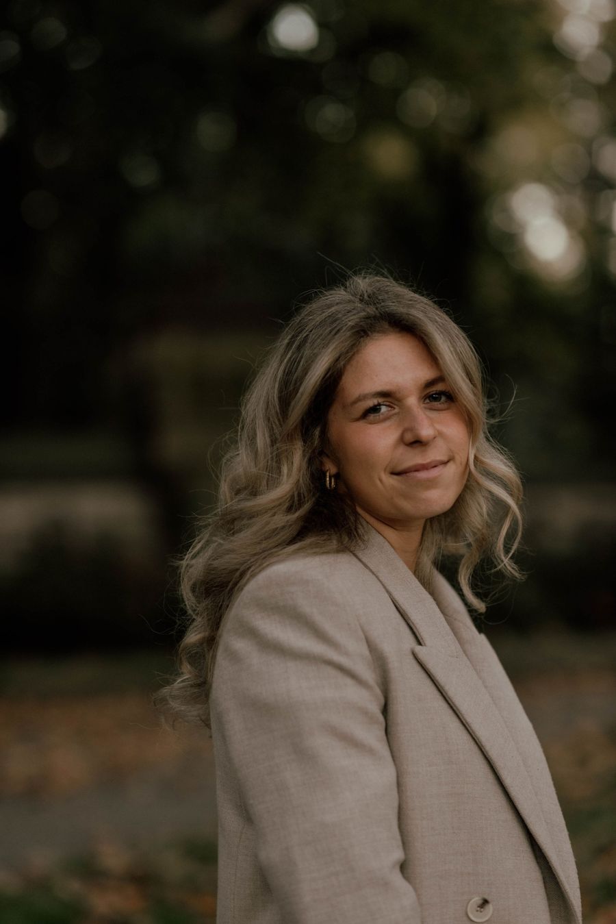 Chana Hirschowitz in a stone-coloured blazer, smiling, among trees